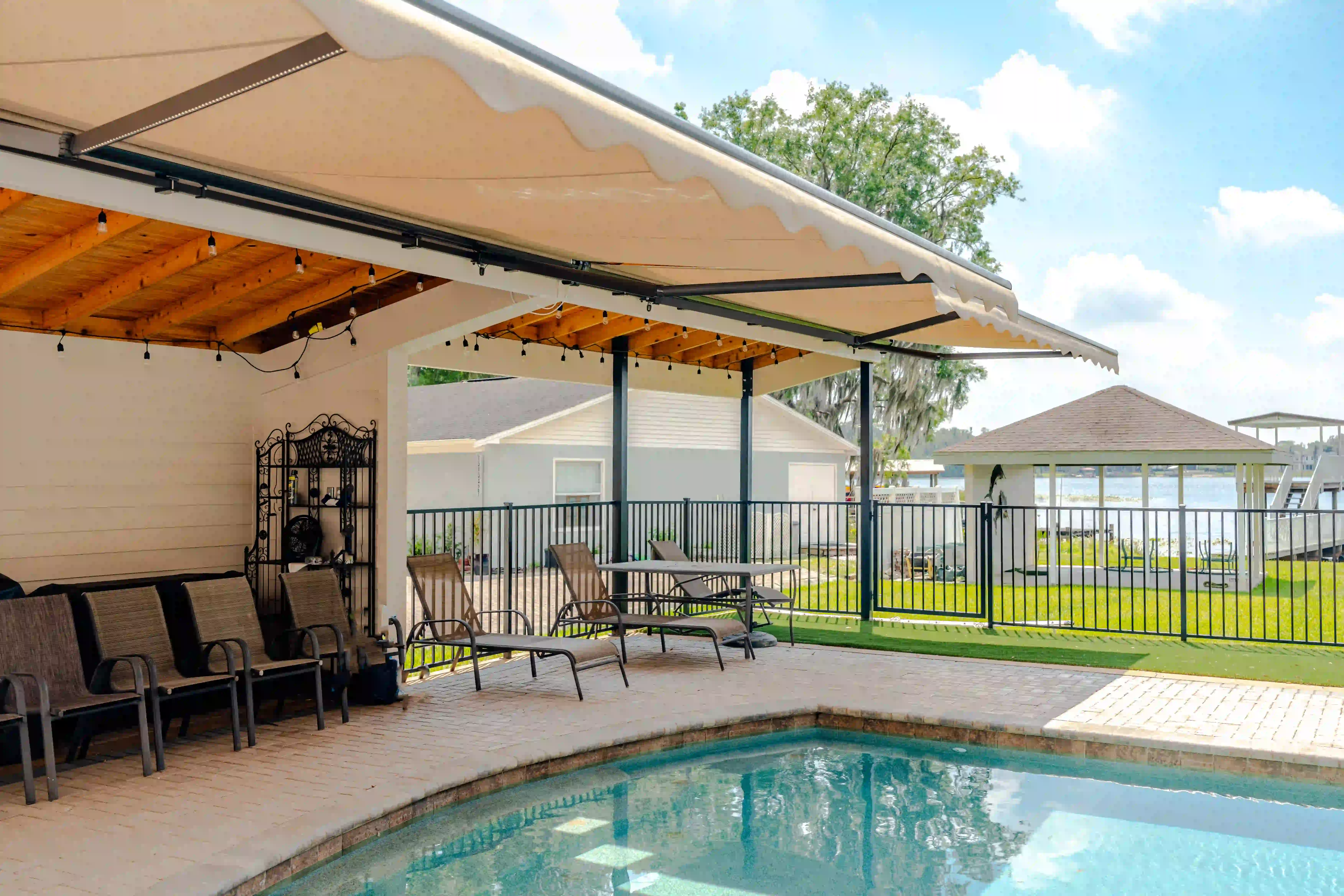 Awning extended over a covered patio and pool with a lake and boat dock visible beyond