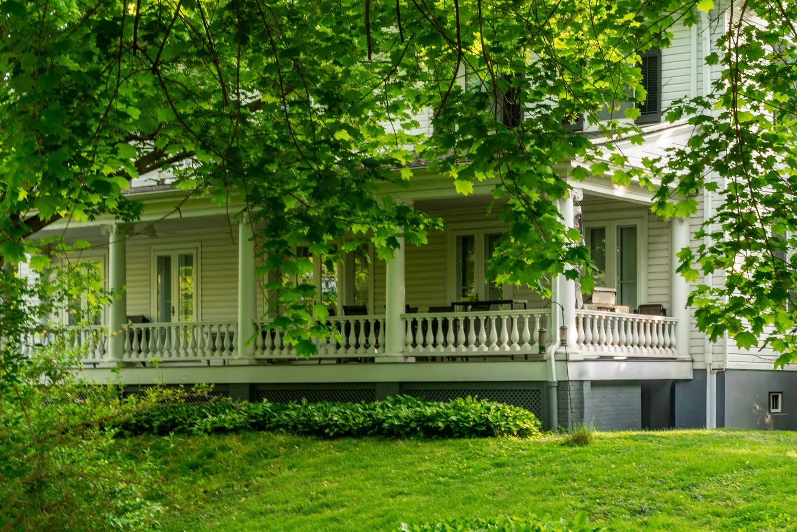 Deeply shaded wraparound porch under mature tree canopy