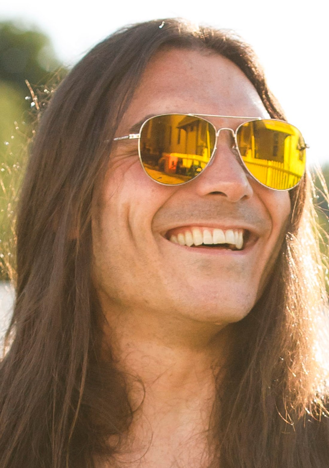 Brandon Yeagley, smiling, long hair, wearing mirrored aviator sunglasses in warm daylight.