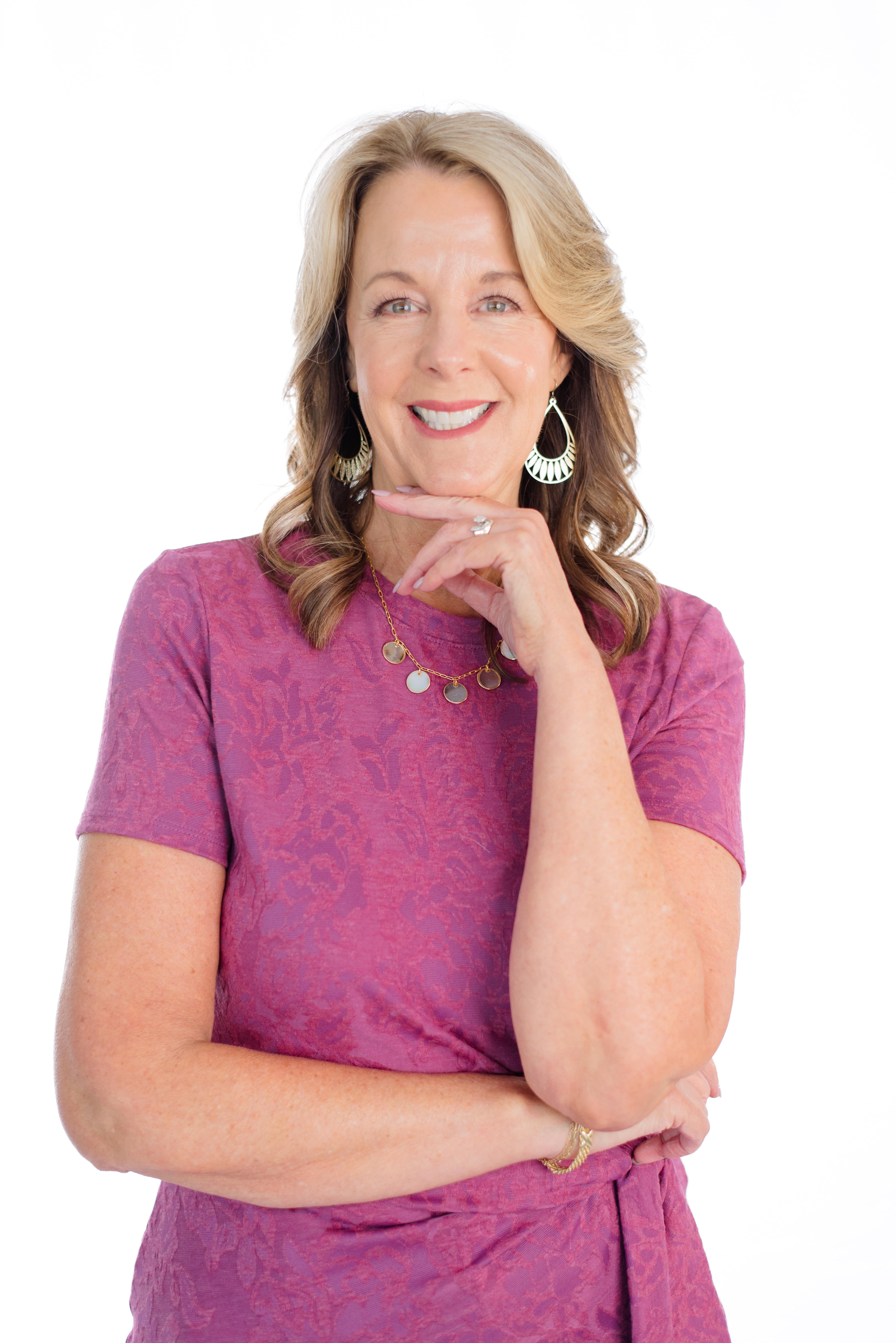 Kathy smiling, resting her chin on her hand, wearing a berry-pink top