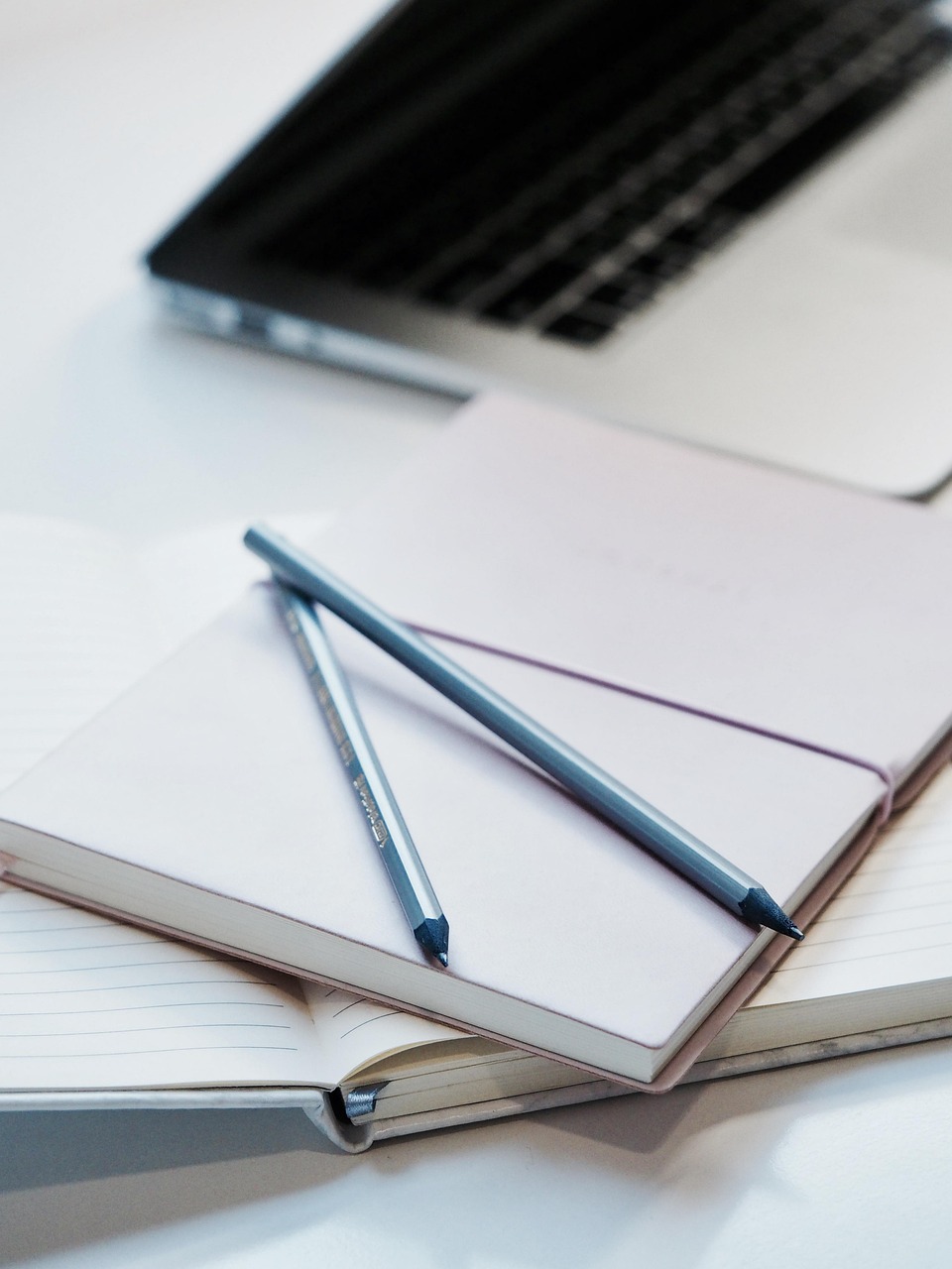 A fountain pen resting on an open notebook on a wooden desk beside books and reading glasses.