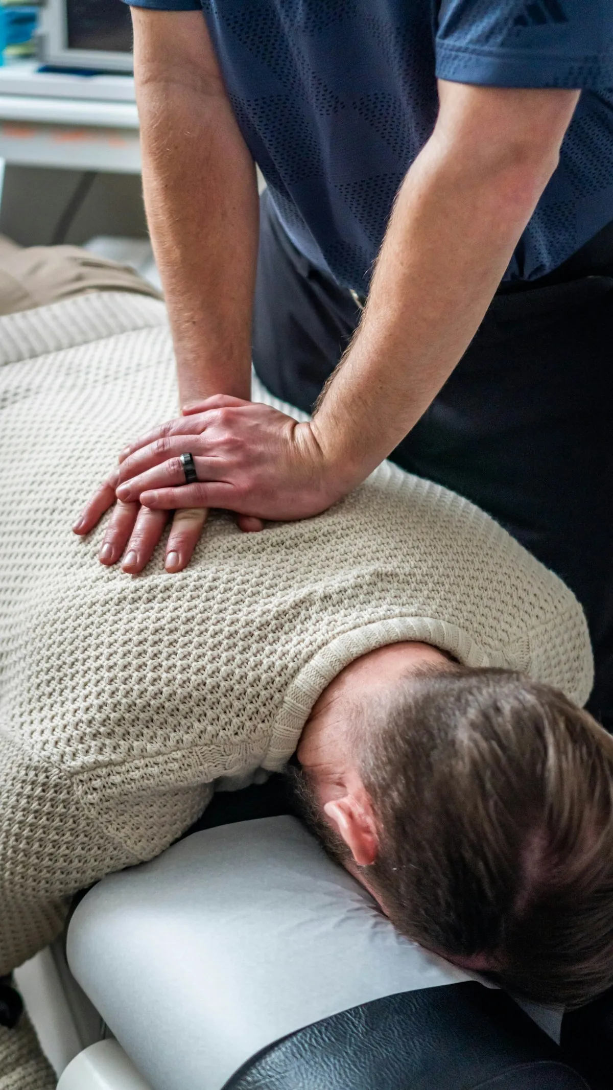 A chiropractor’s hands on a patient’s upper back