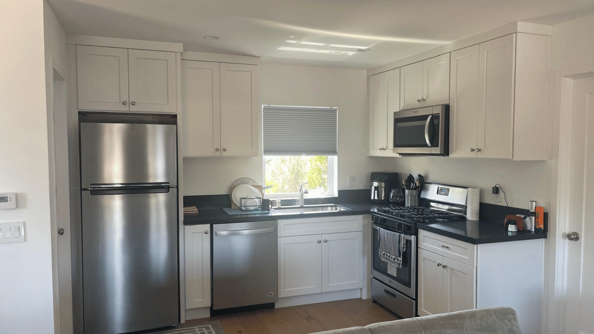 Compact, modern kitchen with white cabinets, stainless steel appliances, and dark countertops.