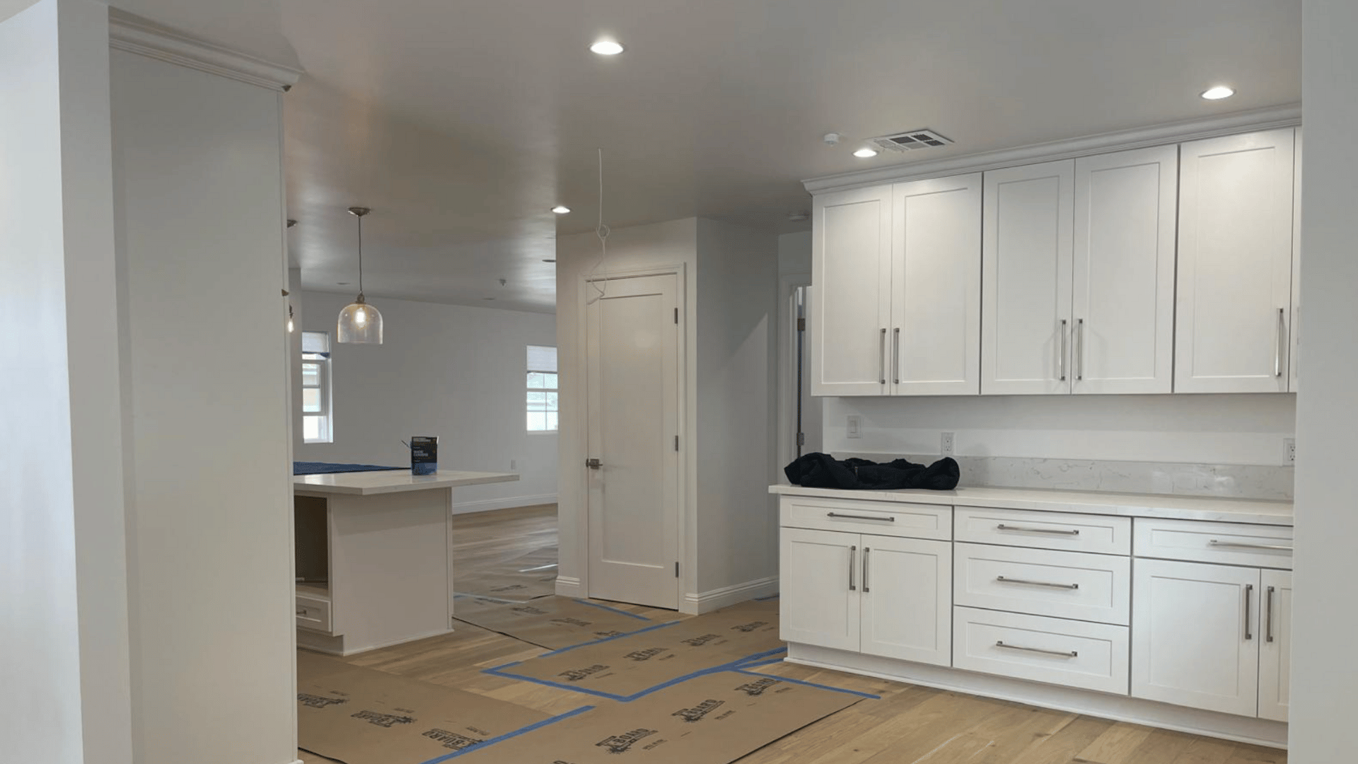 Open-concept kitchen under construction with white cabinetry, stainless steel appliances, and natural wood flooring.