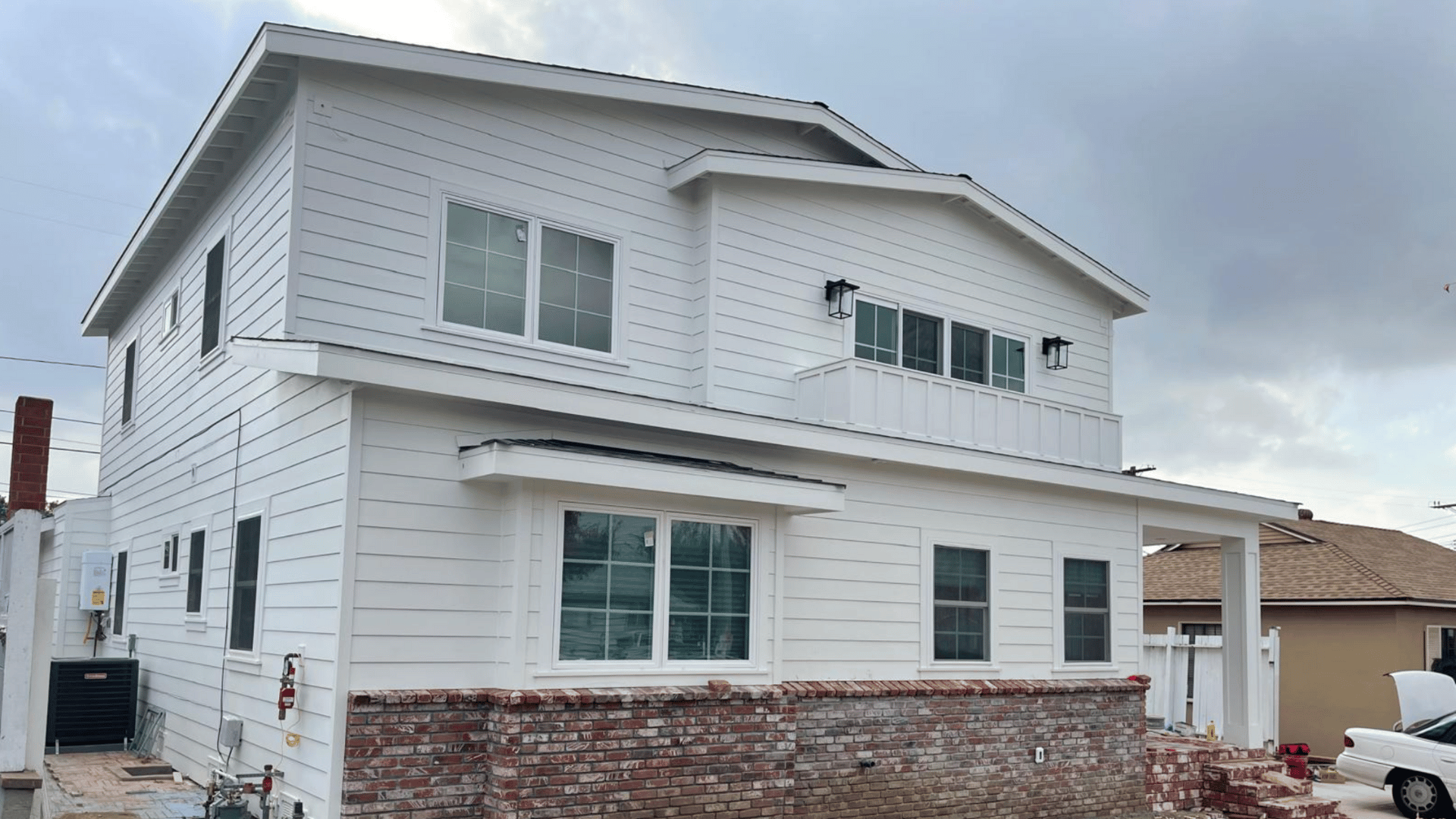  Modern two-story white house with brick detailing on the lower exterior, featuring large windows and a small balcony.