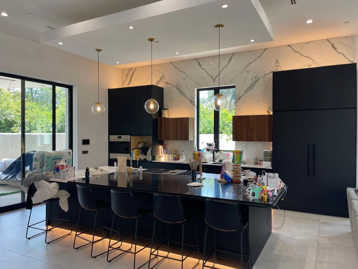 Contemporary kitchen with dark wood cabinets, marble backsplash, and pendant lighting over a large island.