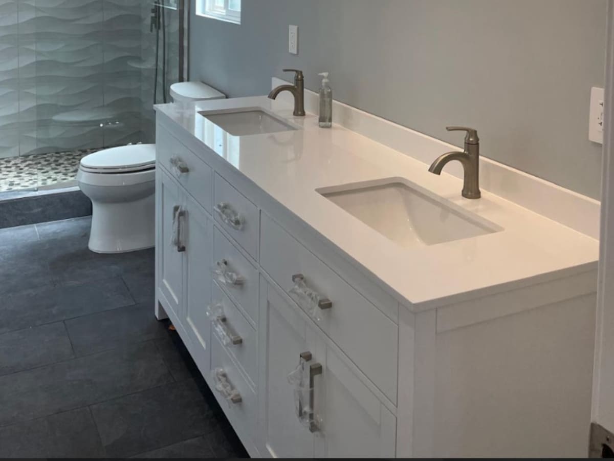 Contemporary bathroom with a double vanity, white countertops, and a glass-enclosed shower with textured wall tiles.