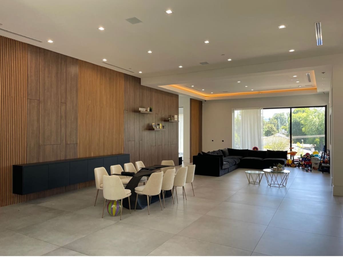 Spacious modern living and dining area with wood-paneled walls, recessed lighting, and large windows providing natural light.