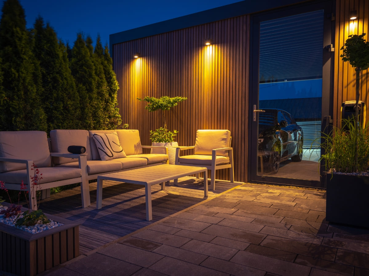 Cozy outdoor seating area with modern furniture, accent lighting, and a wooden panel backdrop, providing a warm ambiance at night.