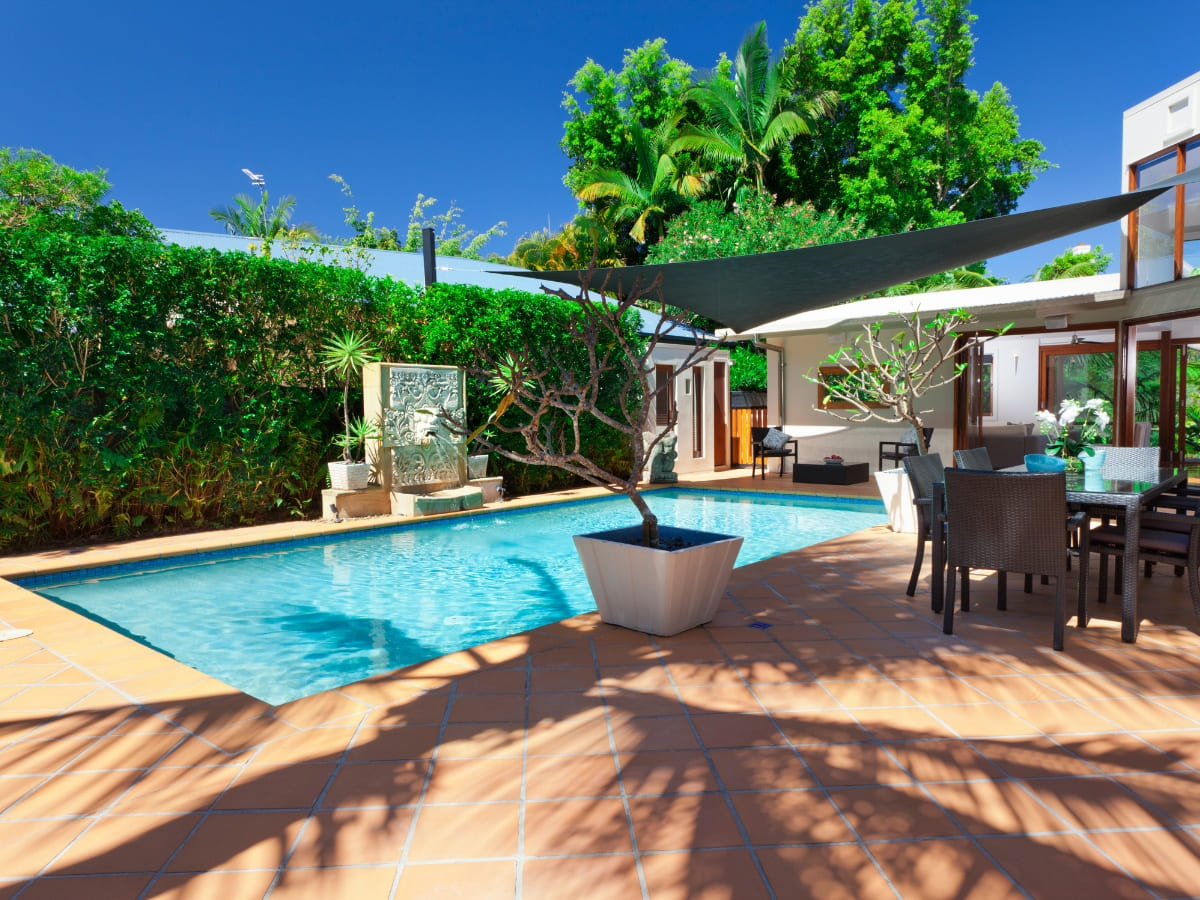 Private backyard pool with a shaded seating area, surrounded by lush greenery and a decorative water feature.