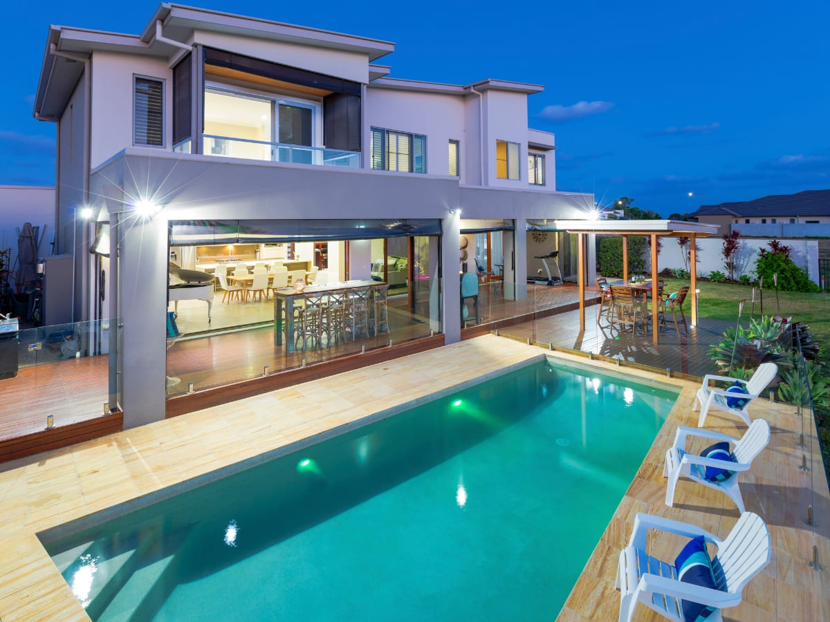 Modern two-story home with a well-lit outdoor pool and a spacious deck area, showcasing a seamless indoor-outdoor living space.