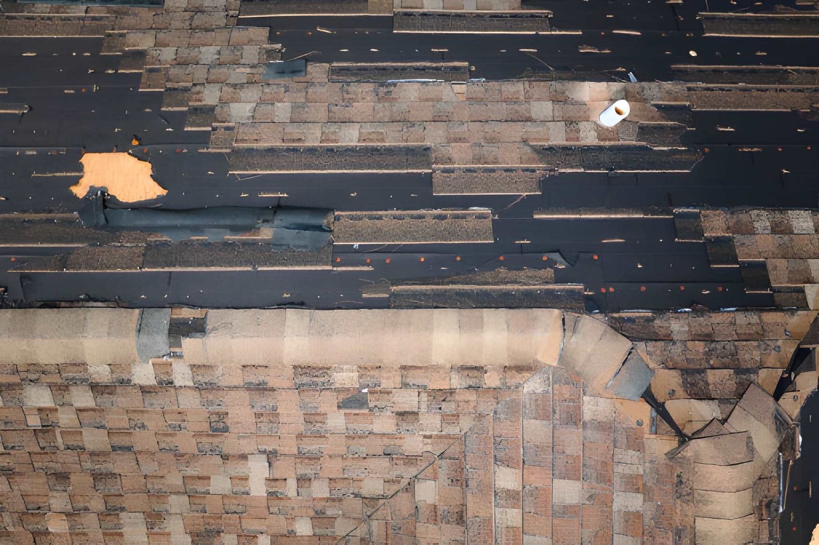 Close-up aerial shot of a torn flat roof showing layered torch-down roofing material and a patched section