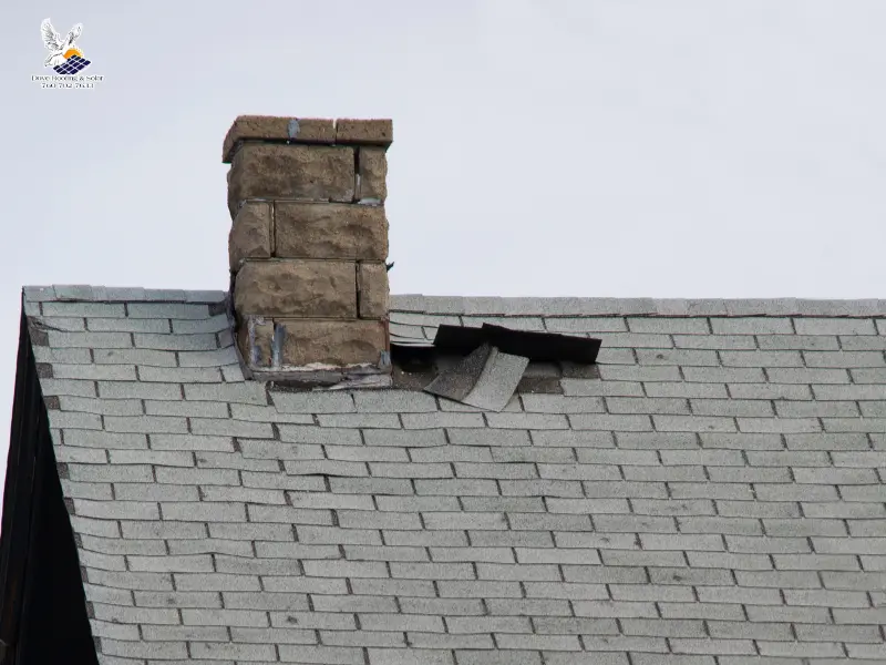 Damaged flashing around a chimney with lifted shingle after storm damage.