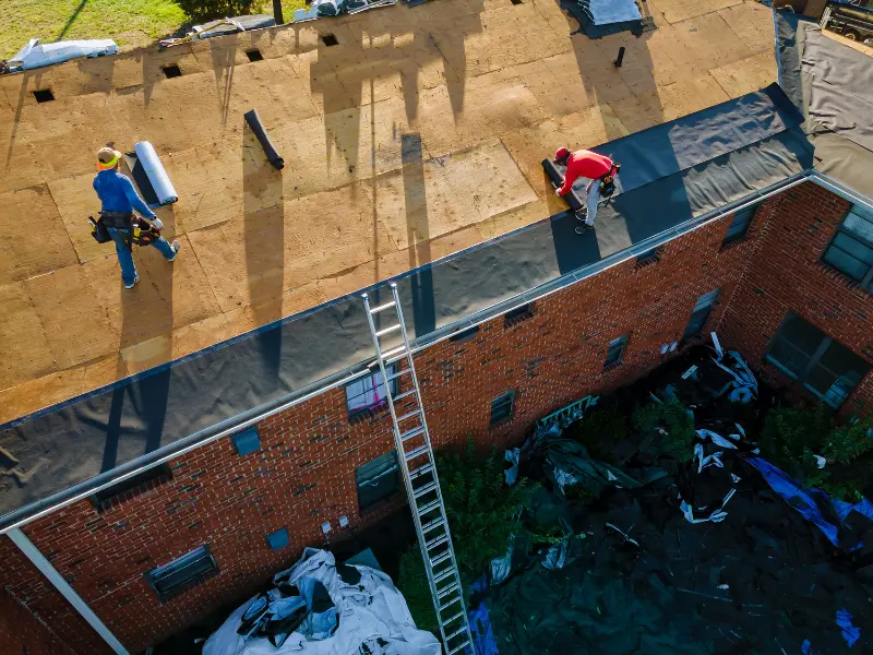 Aerial view of two roofers installing a flat roof membrane on a commercial building