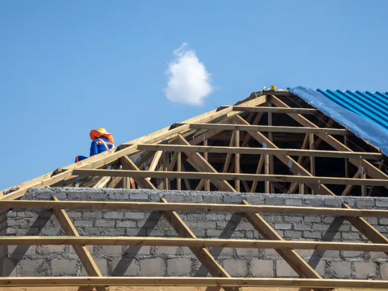 Worker installing wood roof trusses on a new construction building