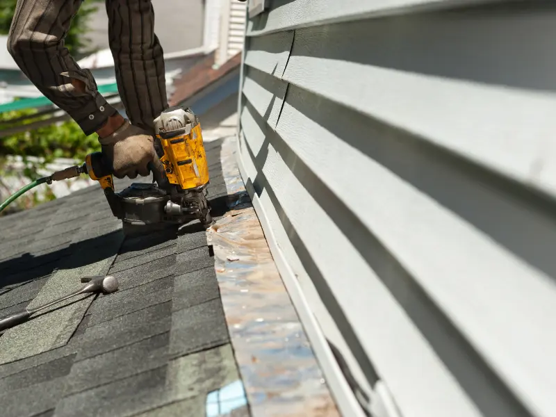 Roofer using a nail gun near the roof edge and house siding