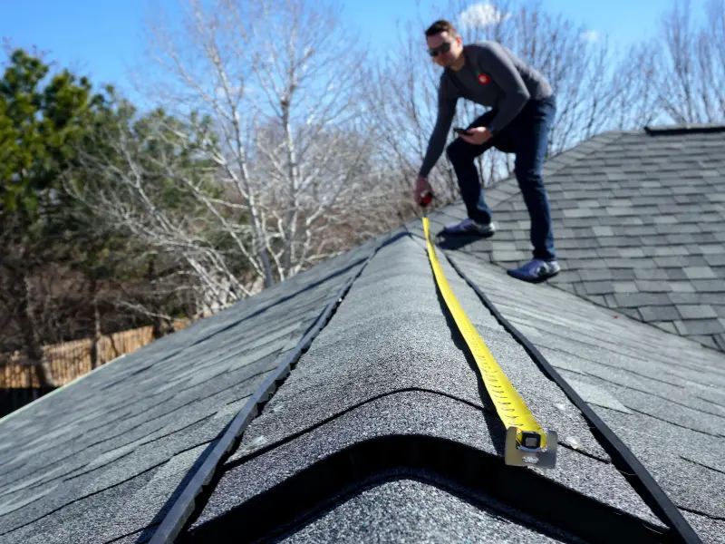 Roofer measuring an asphalt shingle roof during an inspection