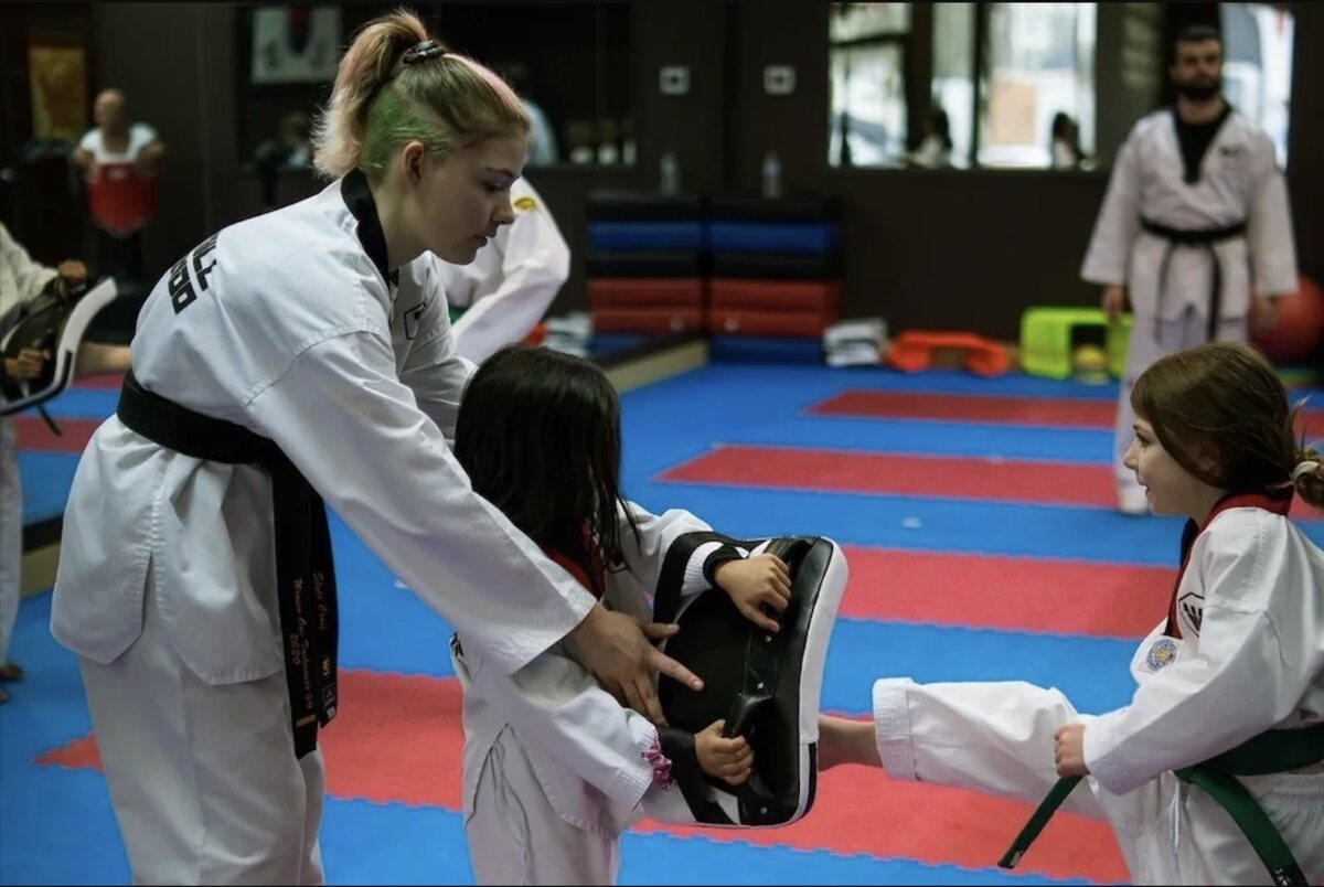 W1 instructor Skyla holding pads for two young students during a drill