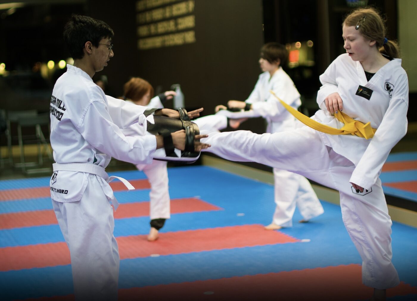 Two teen students drilling a kick on a pad at W1 Taekwondo, mid strike