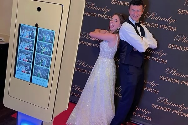 Two teenagers posing beside a PhotoBot booth at prom
