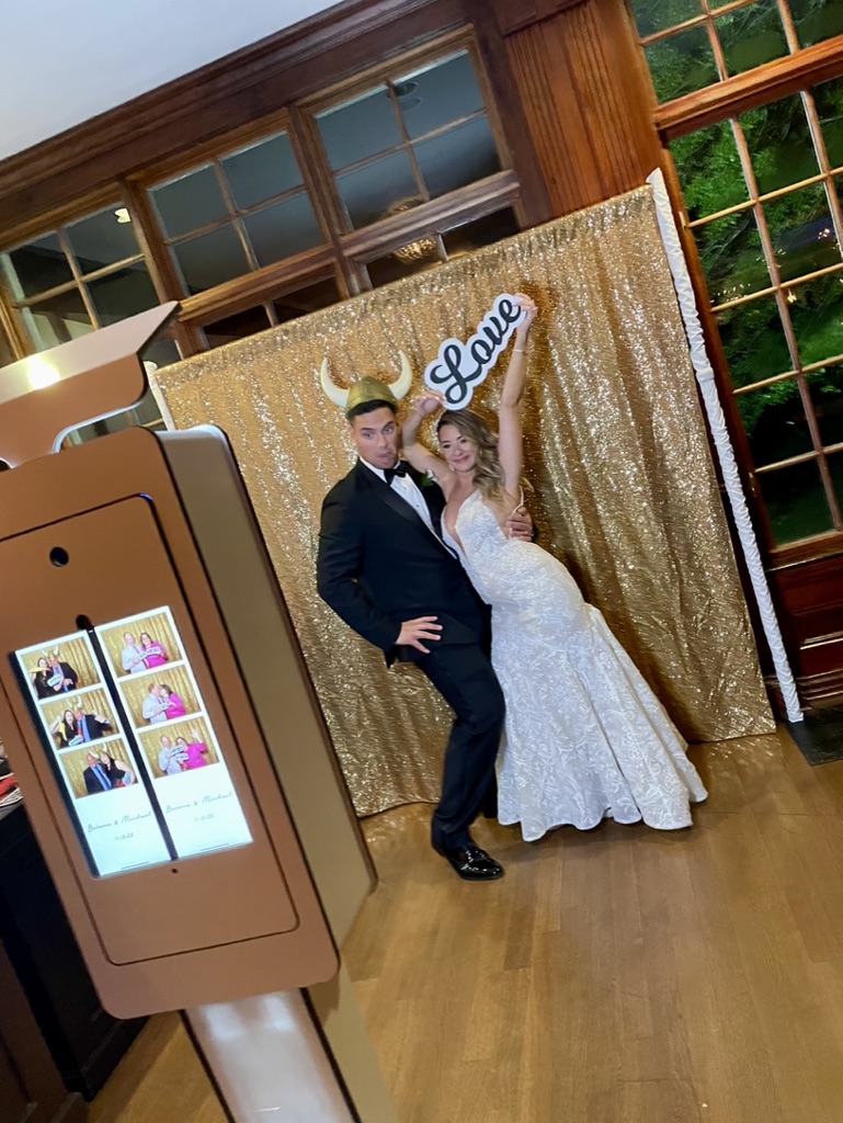 Couple posing in front of a gold sequin backdrop at an open air photo booth