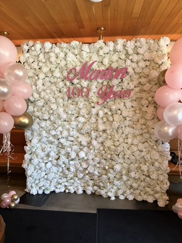 White flower wall backdrop with balloons and a custom name sign