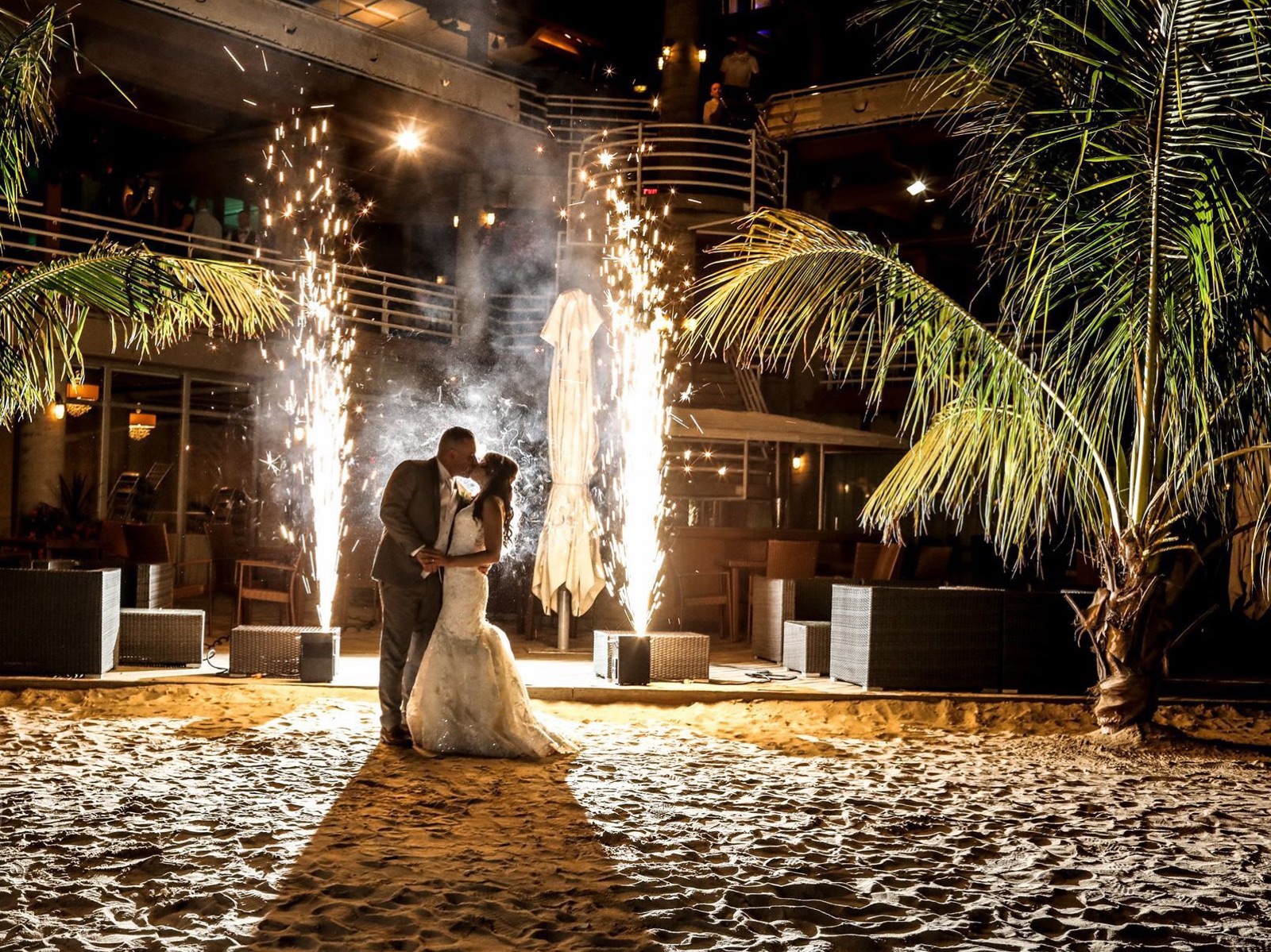 Cold spark fountains behind a couple at a beach reception