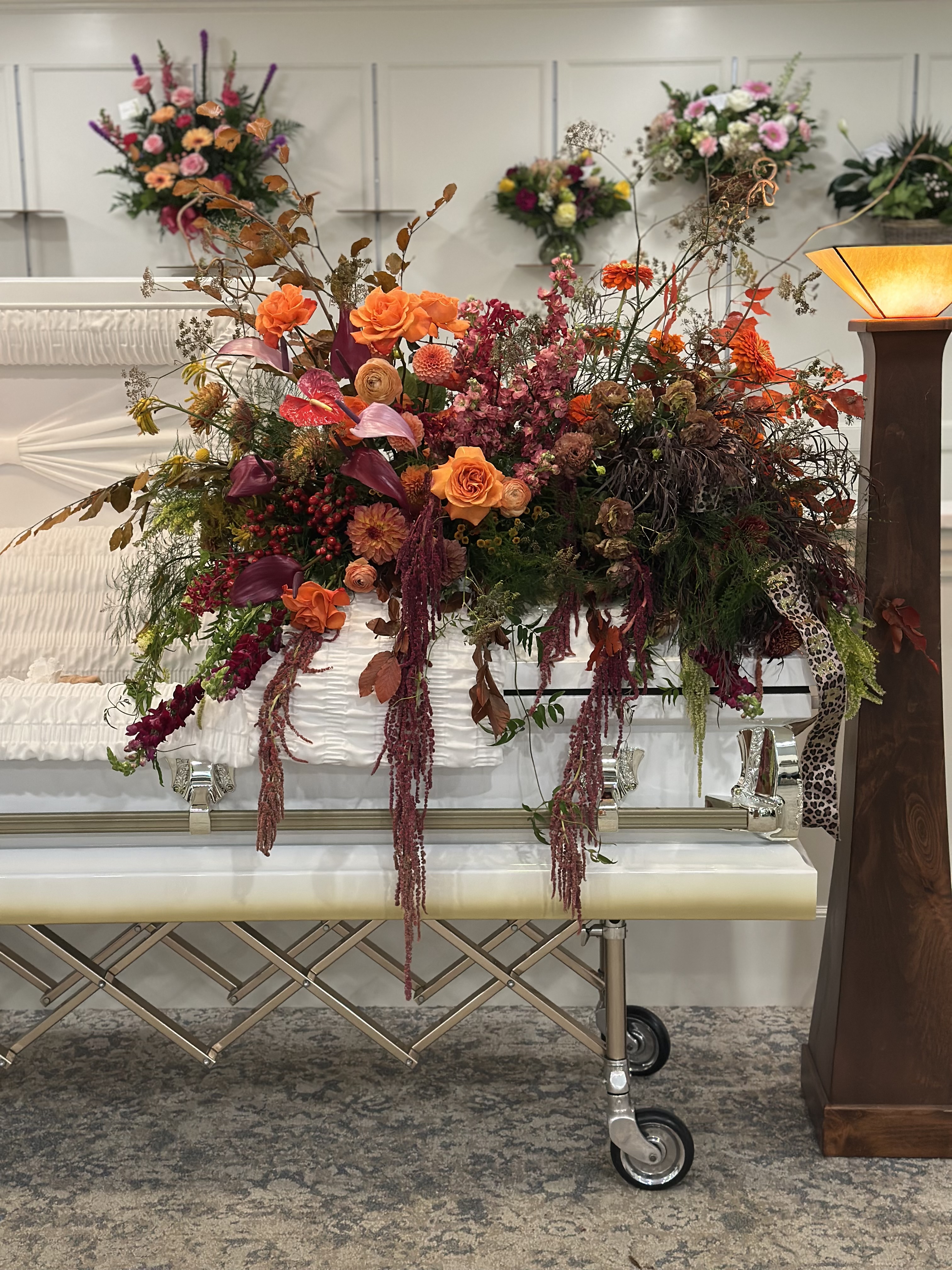 Cascading casket spray of orange roses, burgundy amaranthus, and autumn florals