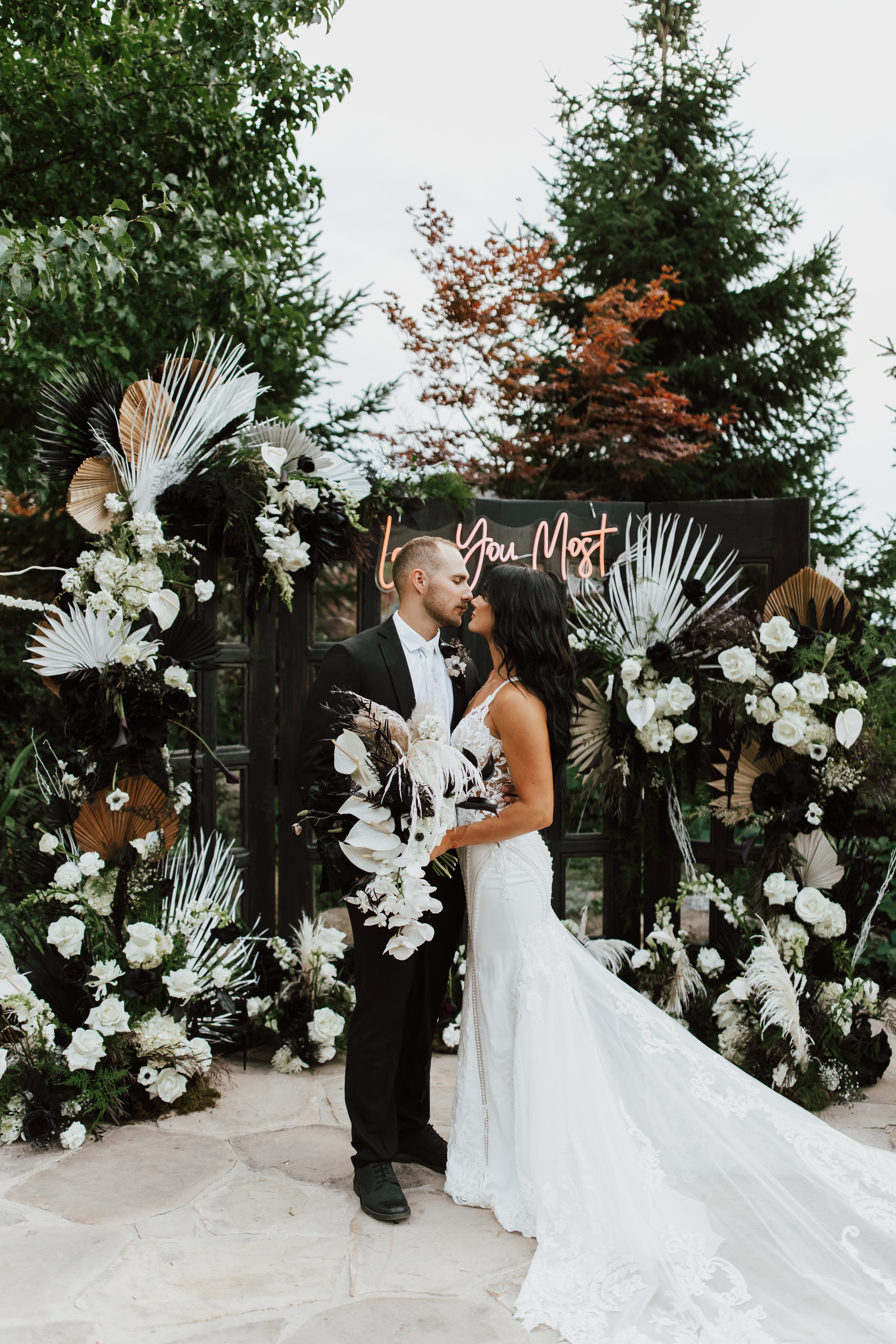 Couple beneath a black and white floral arch among the pines