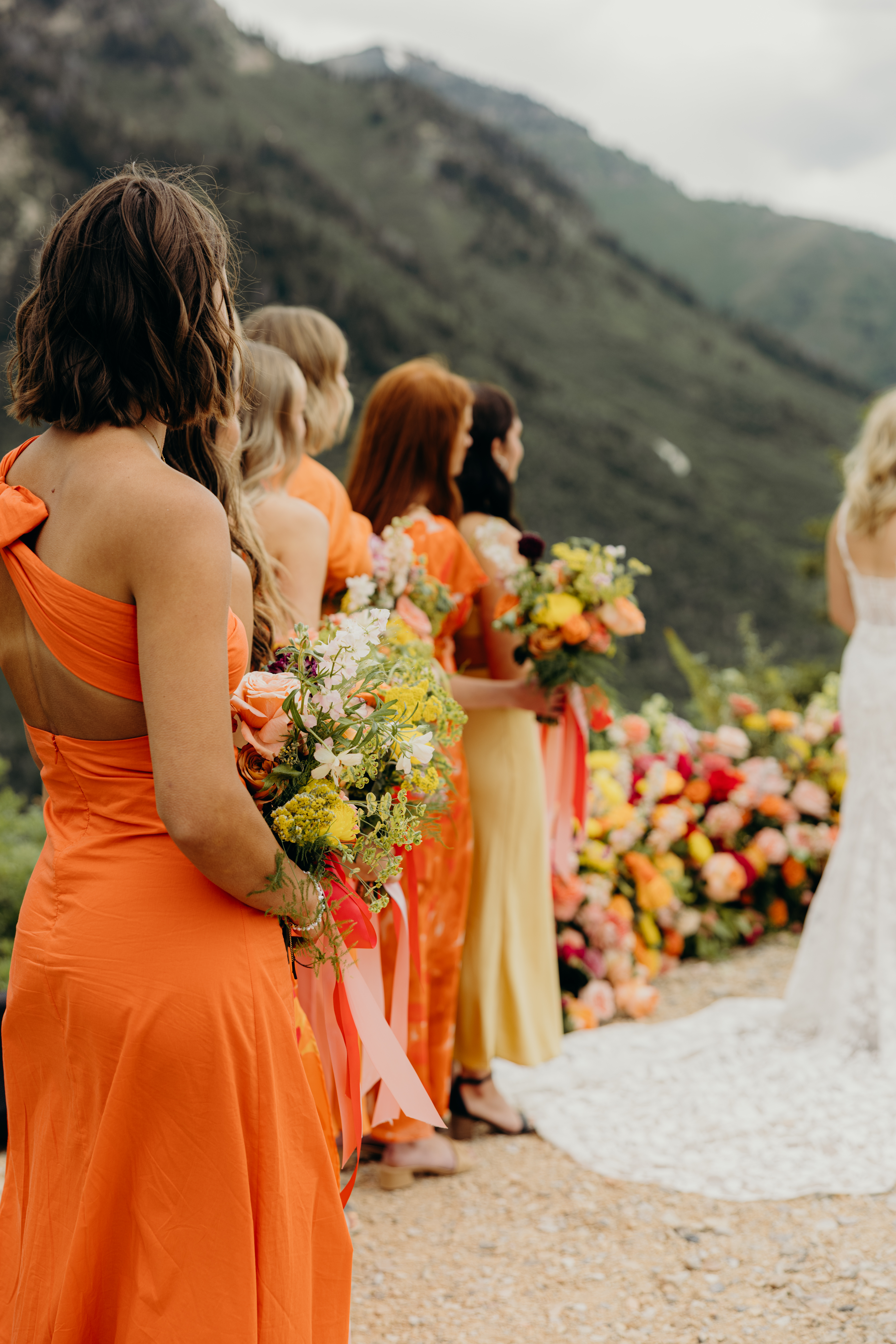 Bridesmaids in orange gowns holding bright bouquets