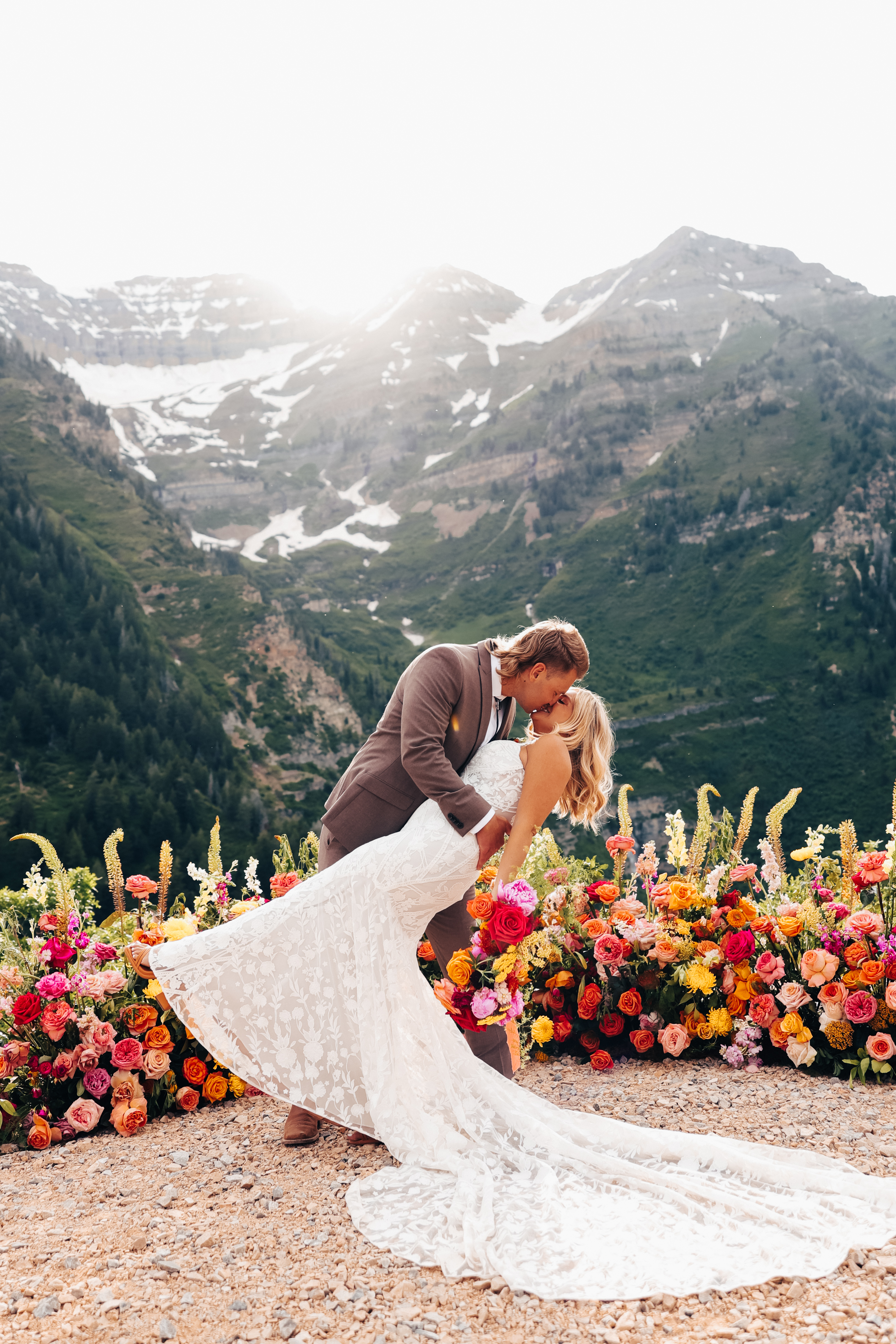 Groom dipping his bride beside a vibrant wildflower installation with Utah mountain peaks behind them