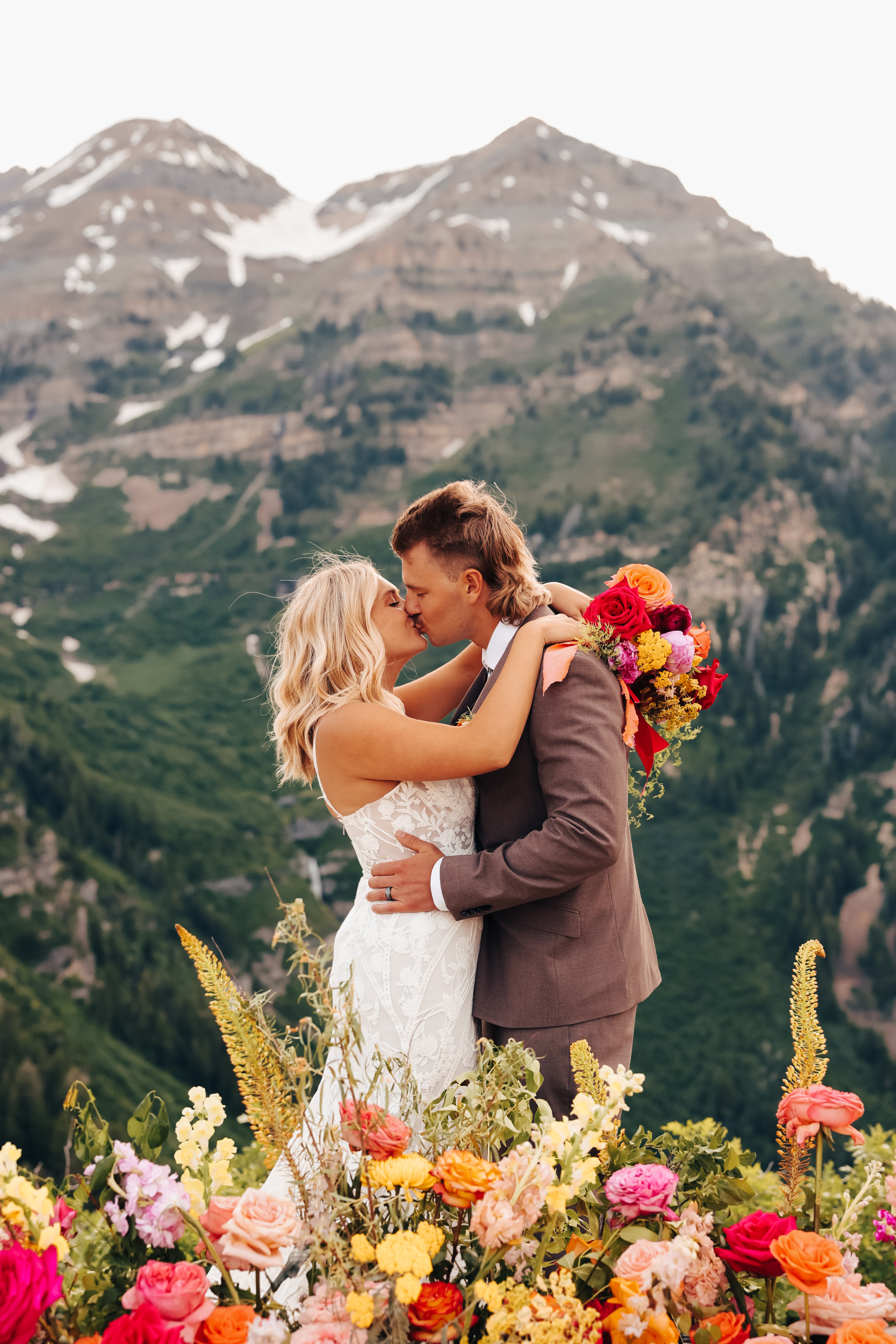 Couple embracing in front of snowcapped peaks and bright florals at Sundance