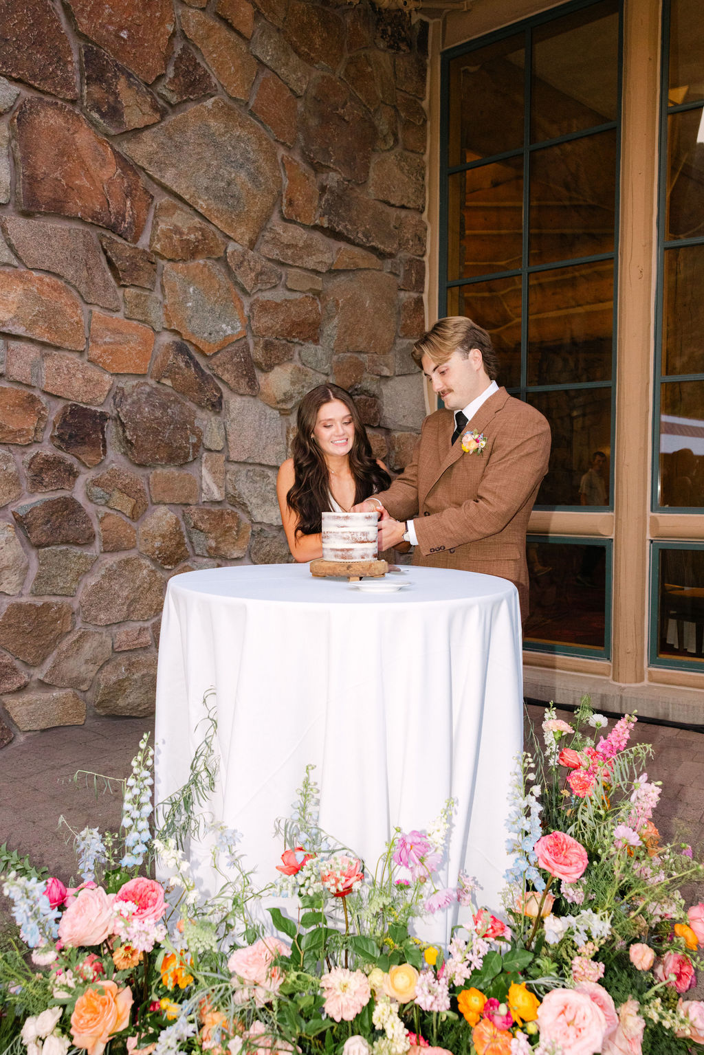 Couple cutting their cake beside a floral-dressed table