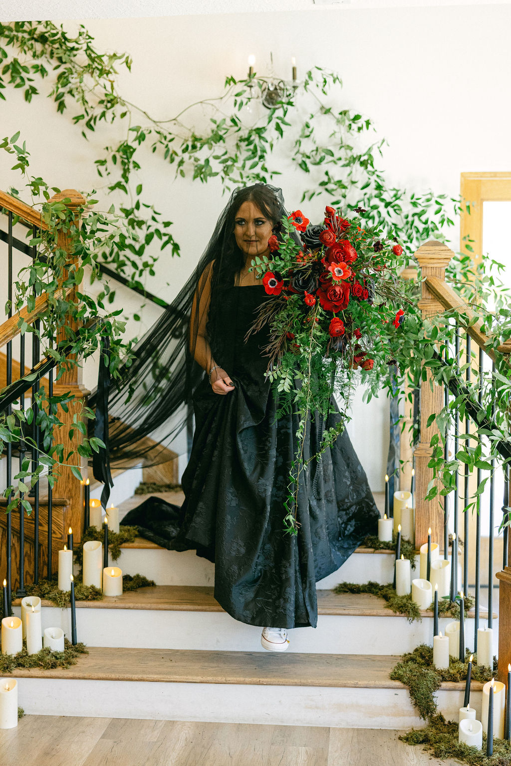 Bride in a black gown on a staircase wrapped in red florals