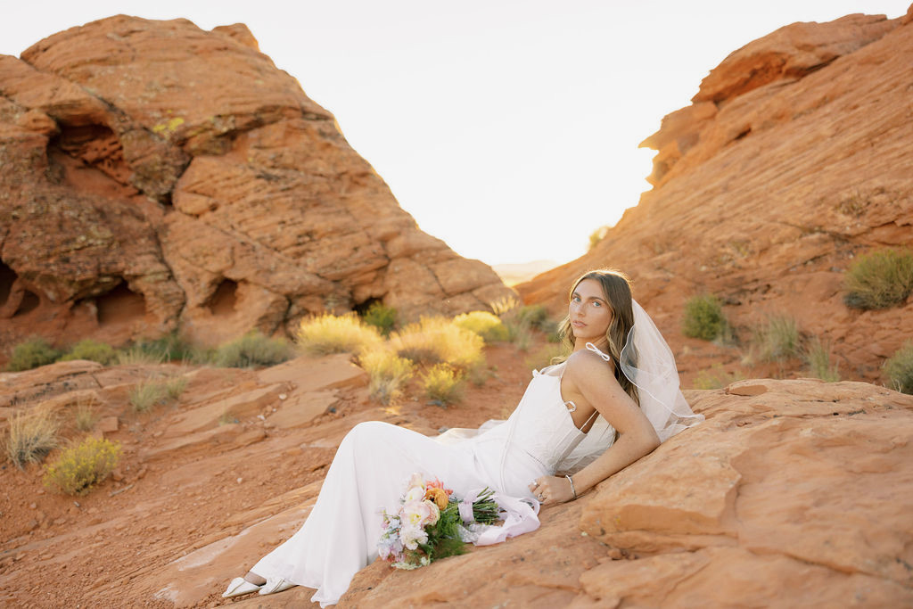 Bride resting on red sandstone with her bouquet