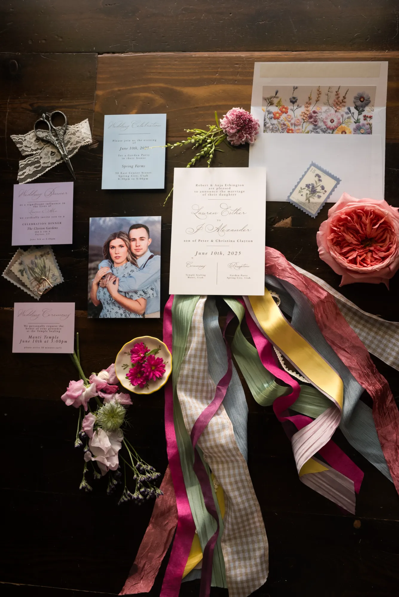 Editorial flat lay of stationery, photos, and ribbon with red blooms