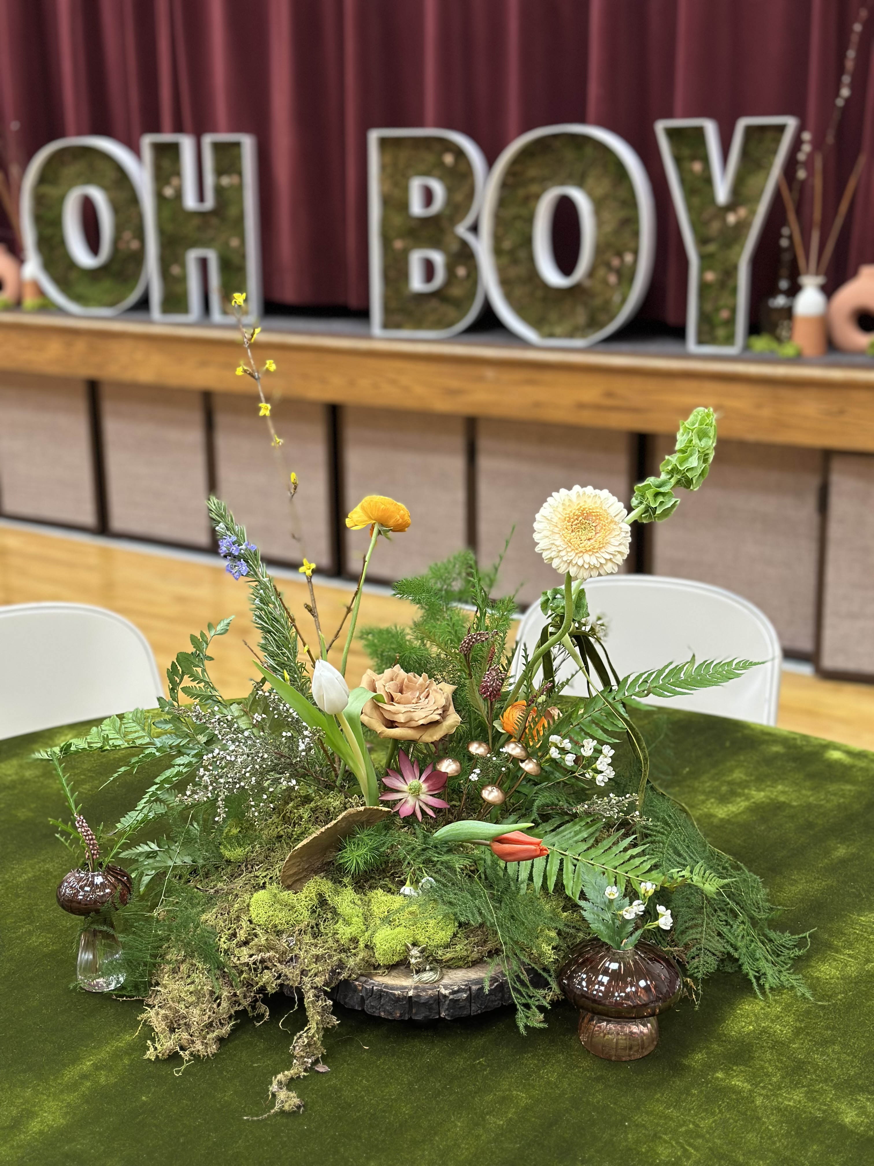 Woodland centerpiece of ferns, moss, and wild blooms on a green velvet table at a baby shower
