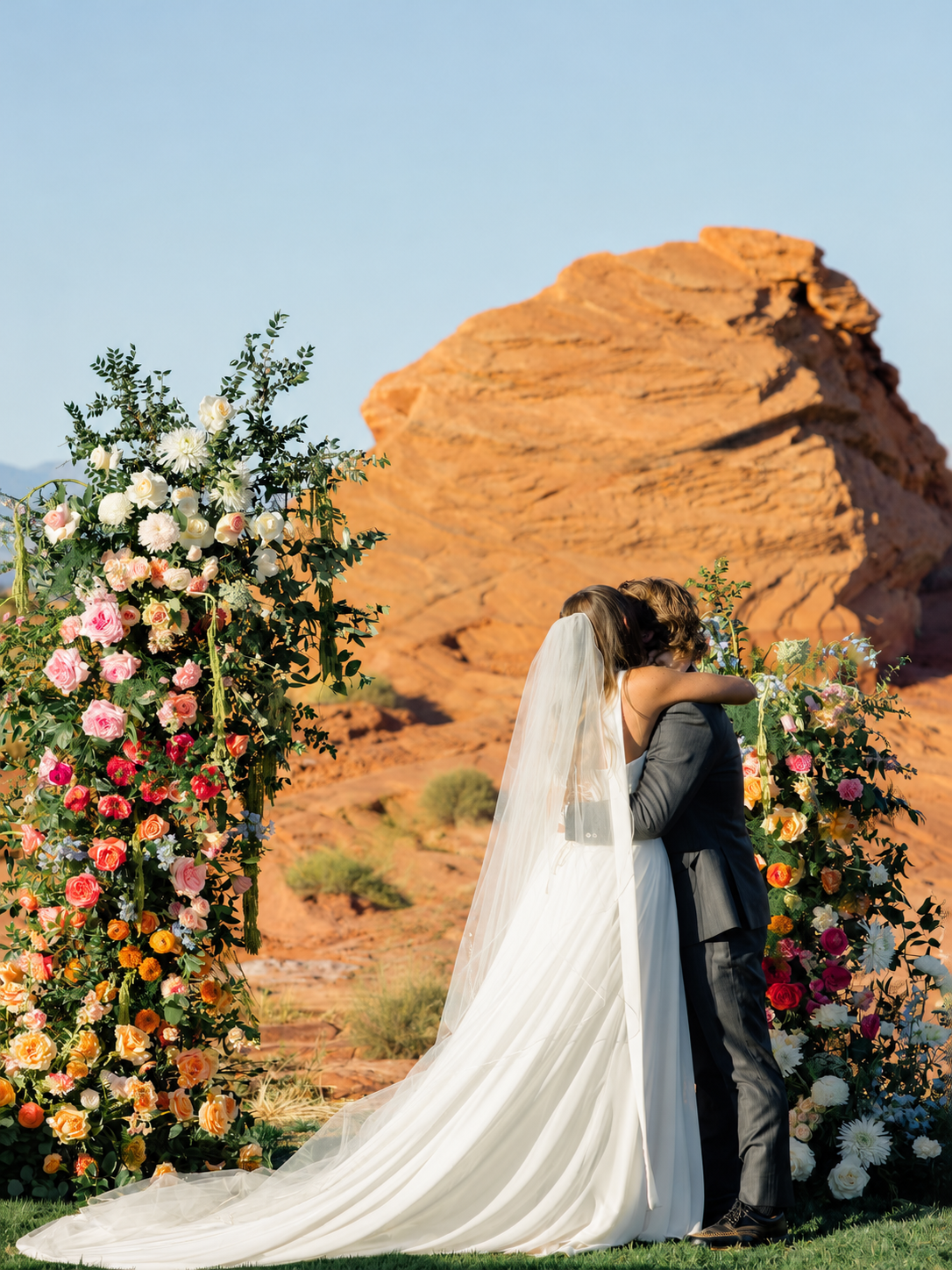 Couple kissing between floral columns and red cliffs