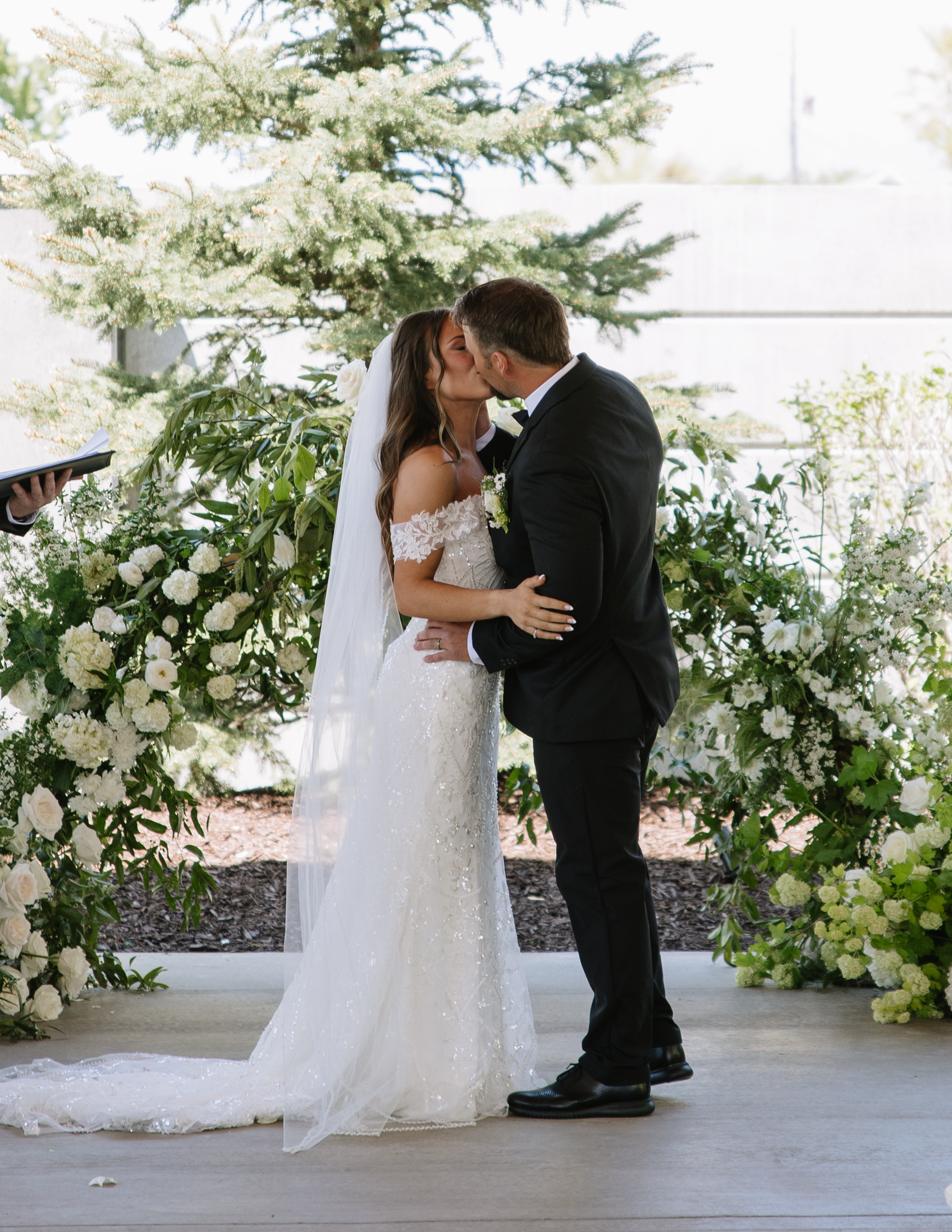 Couple kissing beneath an ivory and green floral arch