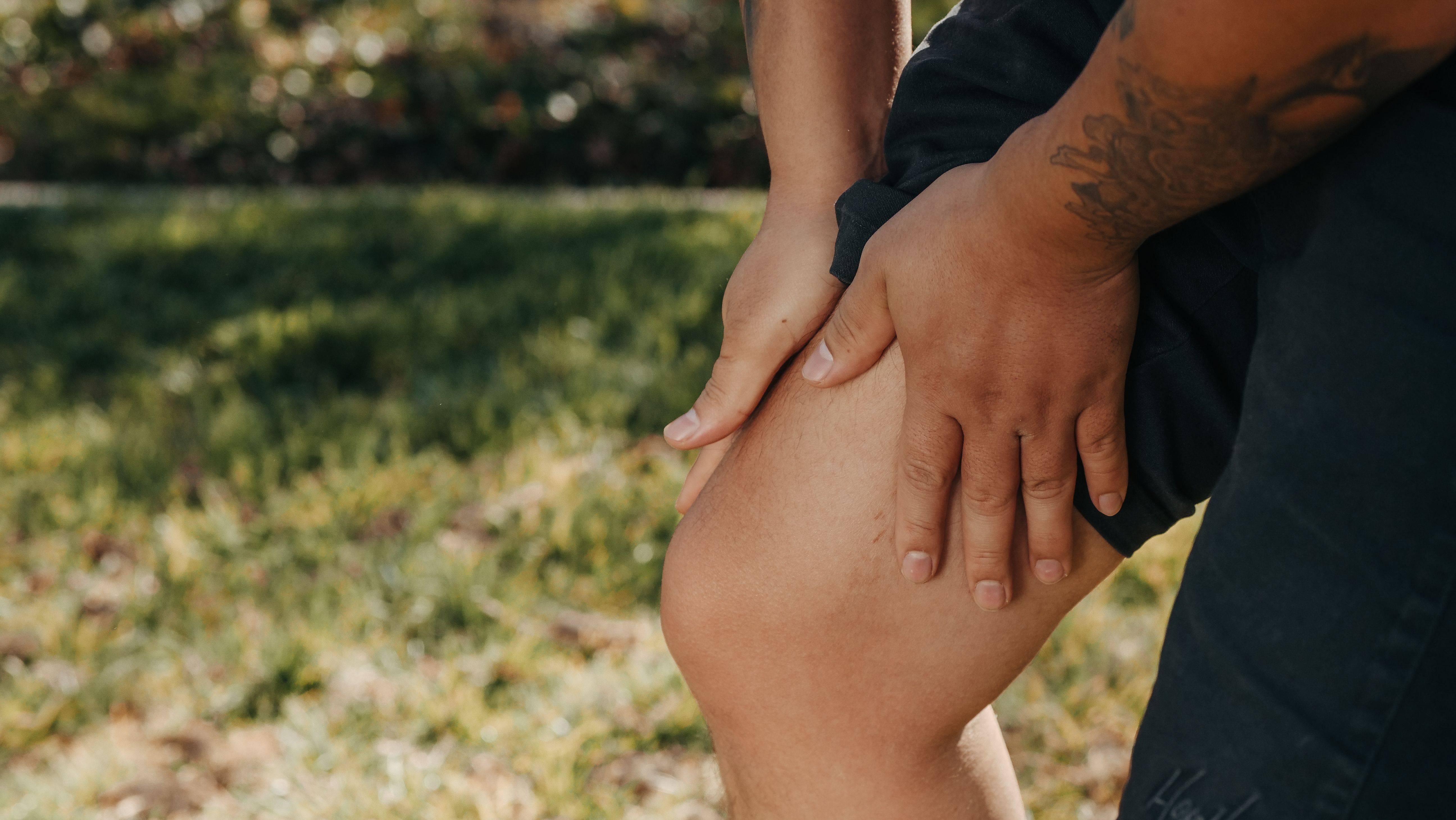 Close-up of a person outdoors gripping a single leg with both hands, illustrating one-sided leg discomfort and swelling.