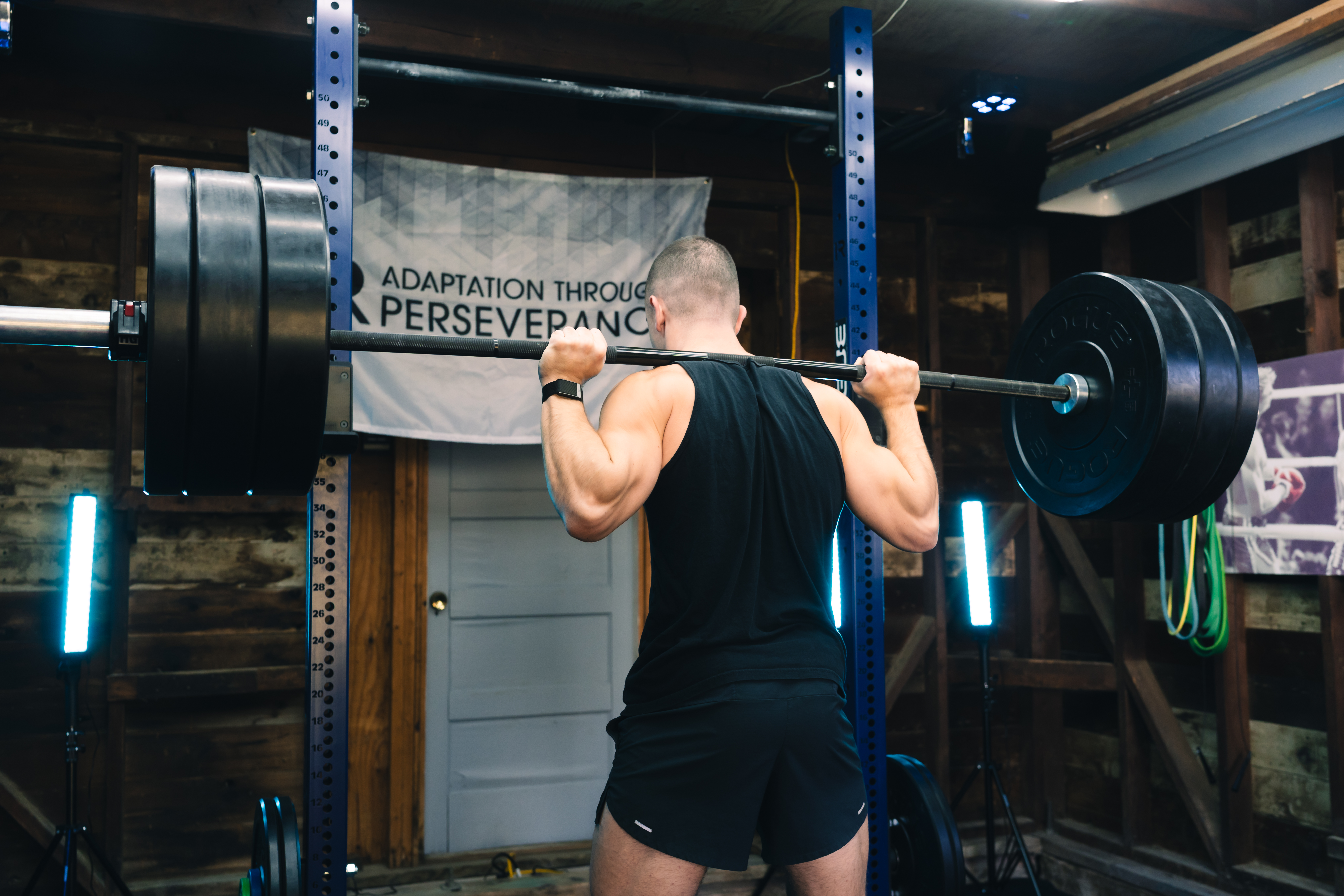Jonathan squatting in his home gym under an Adaptation Through Perseverance banner
