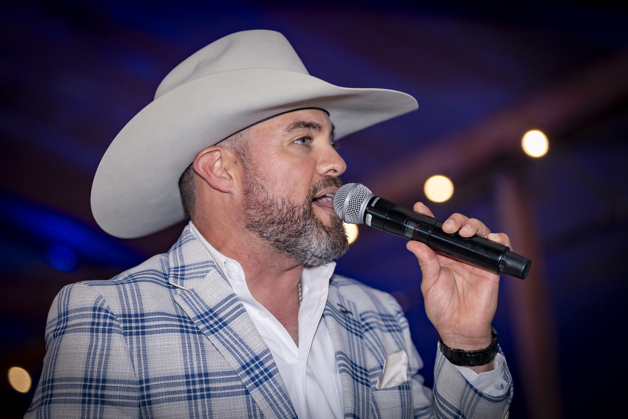 Ferron wearing a cowboy hat, speaking into a microphone