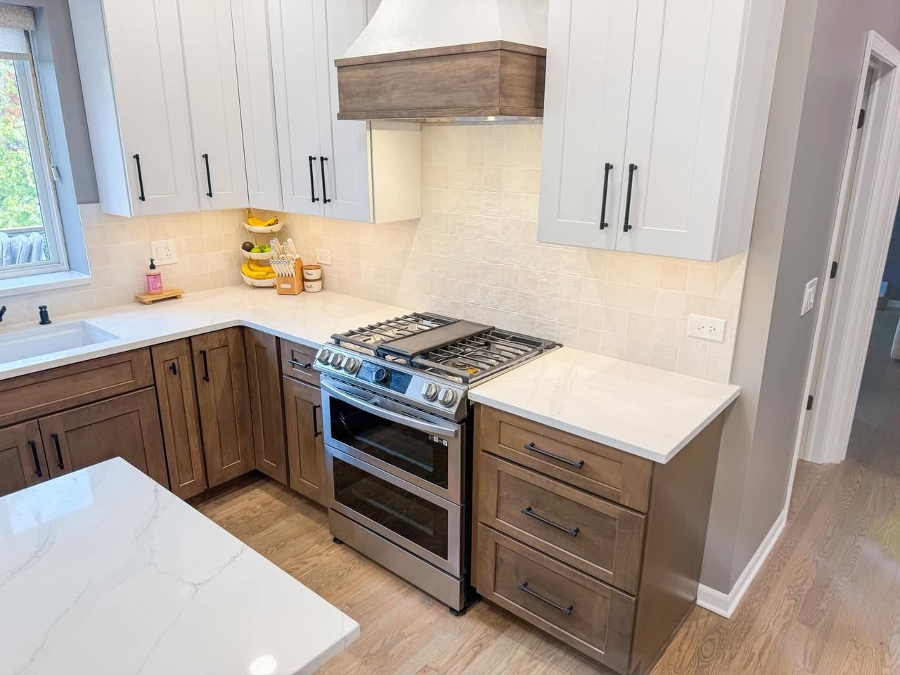 White upper cabinets over stained wood lower cabinets, a wood-banded range hood, square tile backsplash and white veined countertops