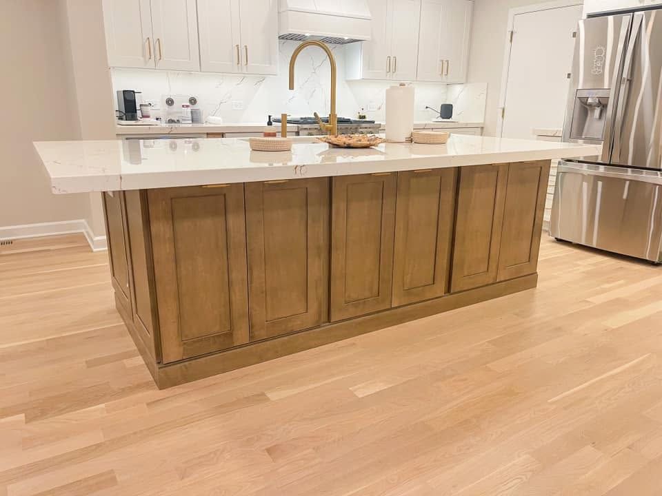 Stained wood kitchen island with a thick white veined countertop and a brass faucet, with white cabinets behind it
