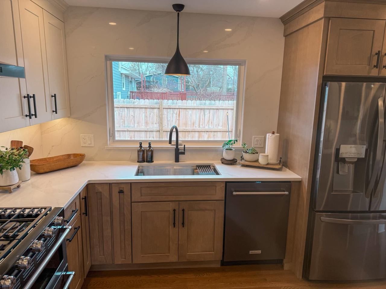 Light-stained shaker cabinets, a full-height veined slab backsplash and a picture window over a stainless steel sink