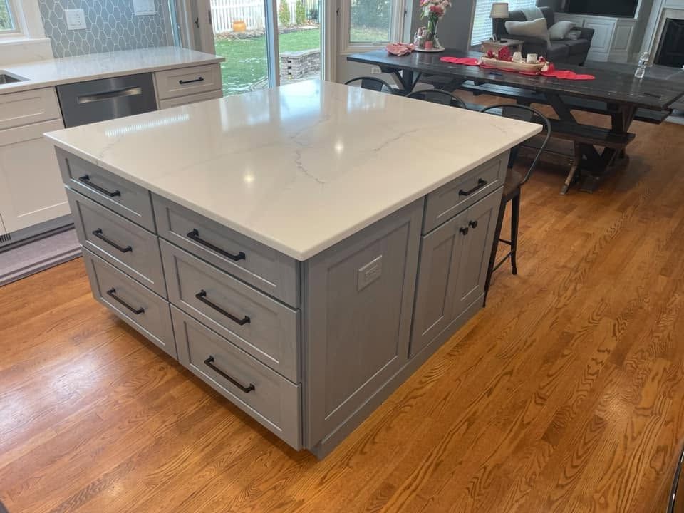 Gray shaker kitchen island with a white veined countertop and black drawer pulls