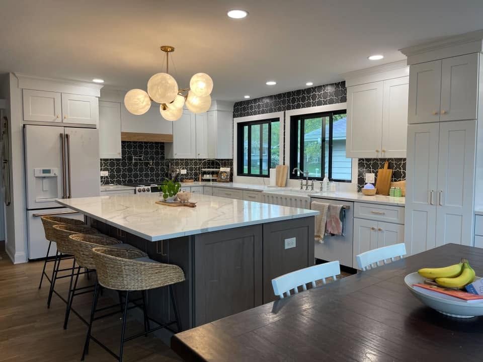 White shaker kitchen with a black patterned tile backsplash, a globe chandelier and a large island with woven counter stools