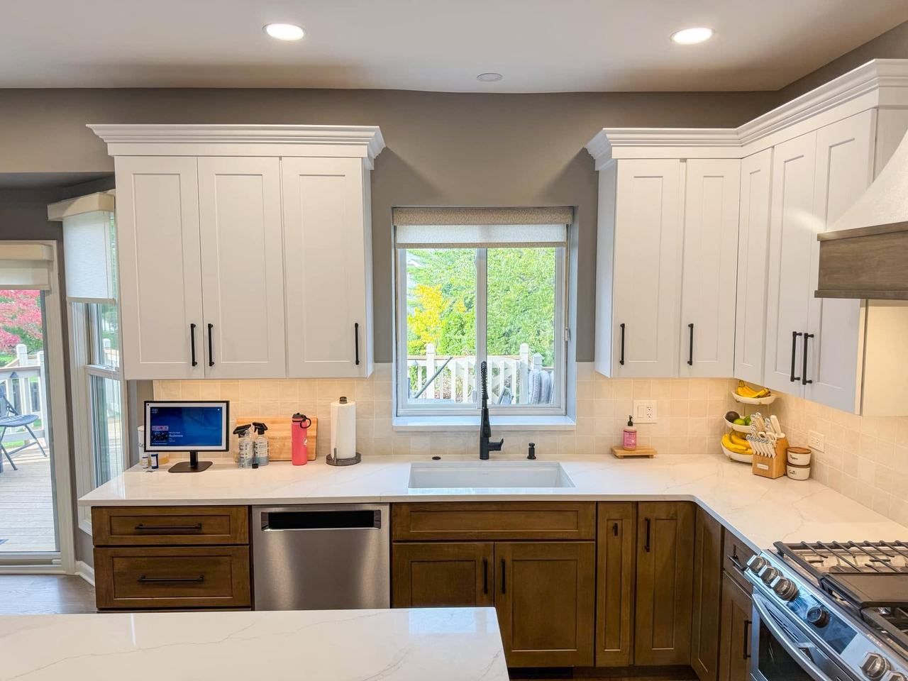 Kitchen sink centered under a white sliding window, with white upper cabinets and stained wood lower cabinets