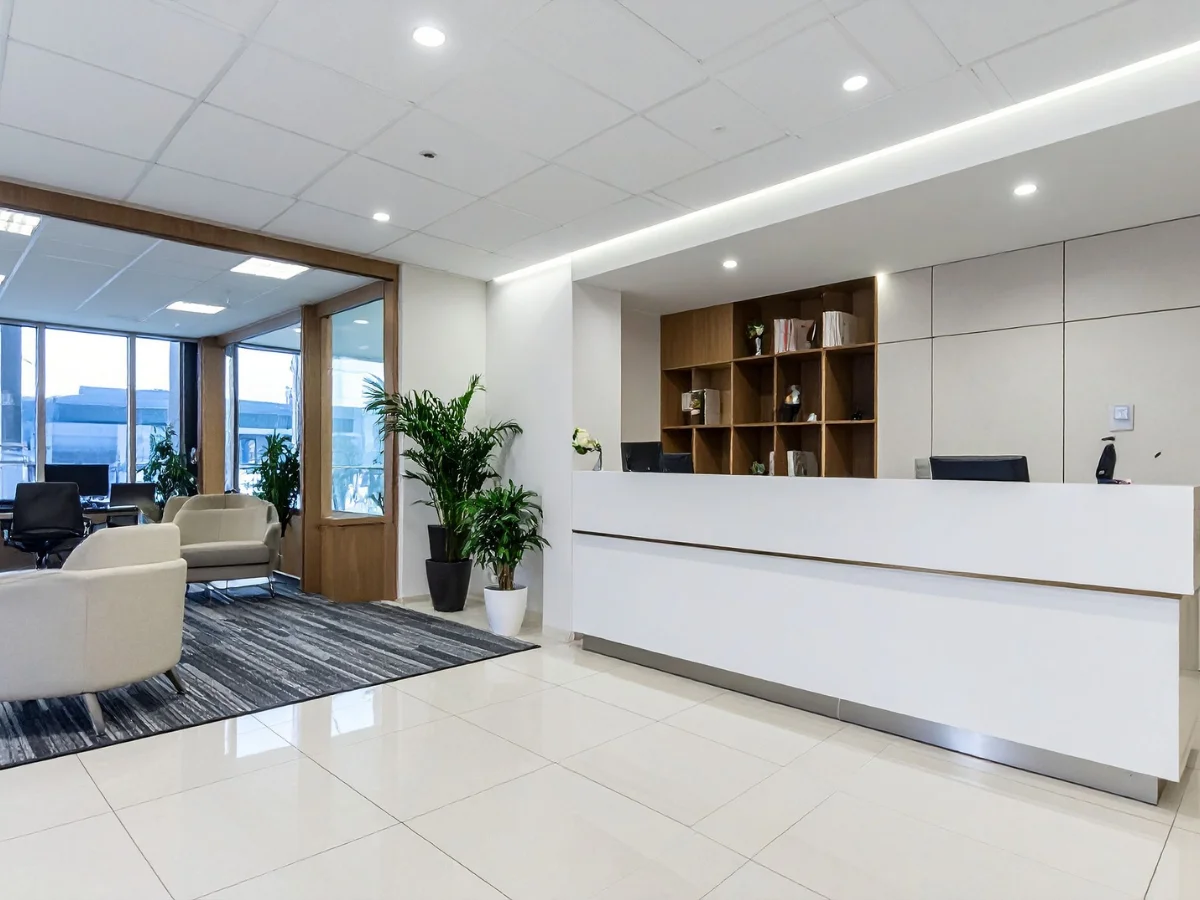 A modern office reception desk with a white counter, wood-paneled wall, and stylish pendant lights.