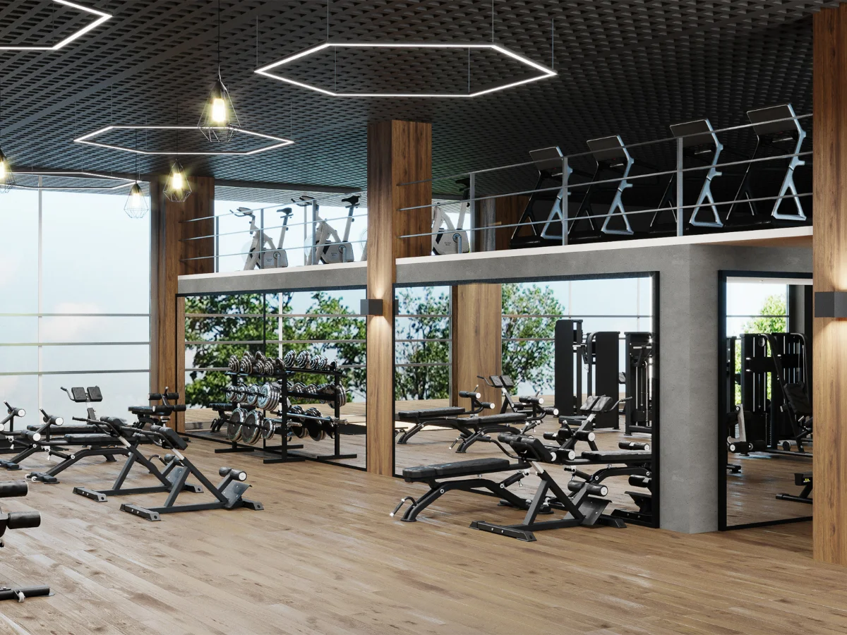 A modern, spacious gym interior with wooden floors, mirrored walls, fitness equipment, and a mezzanine with cardio machines.